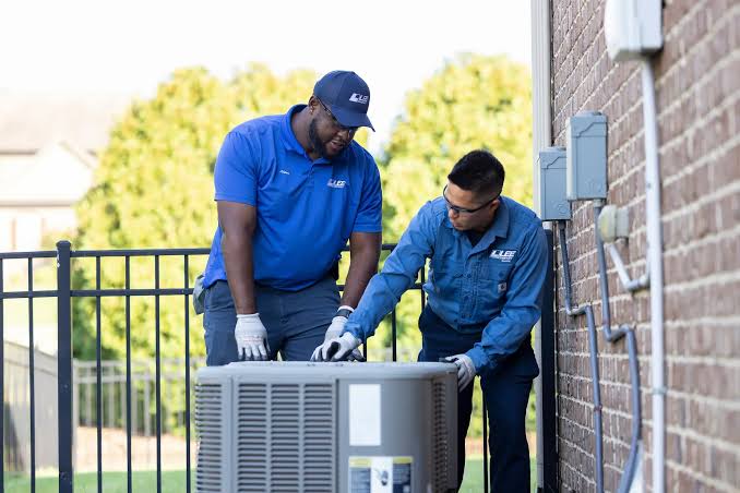 Two HVAC technicians installing a residential outdoor cooling unit