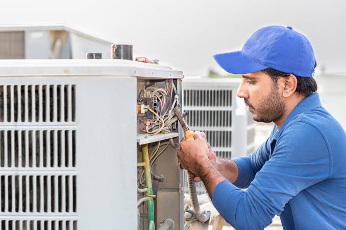 HVAC technician repairing electrical components in an outdoor unit